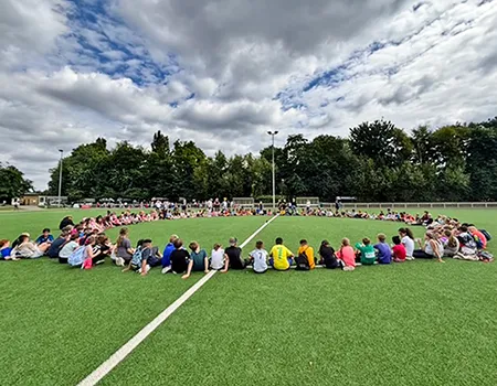 Kinder im großen Sitzkreis auf dem Sportplatz