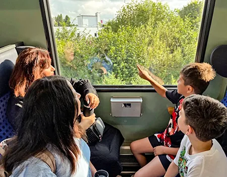 Eine Gruppe von Kindern sitzt mit einem Erwachsenen im Zugabteil