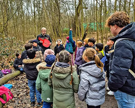 Kinder hören im Wald den Erläuterungen des Försters zu